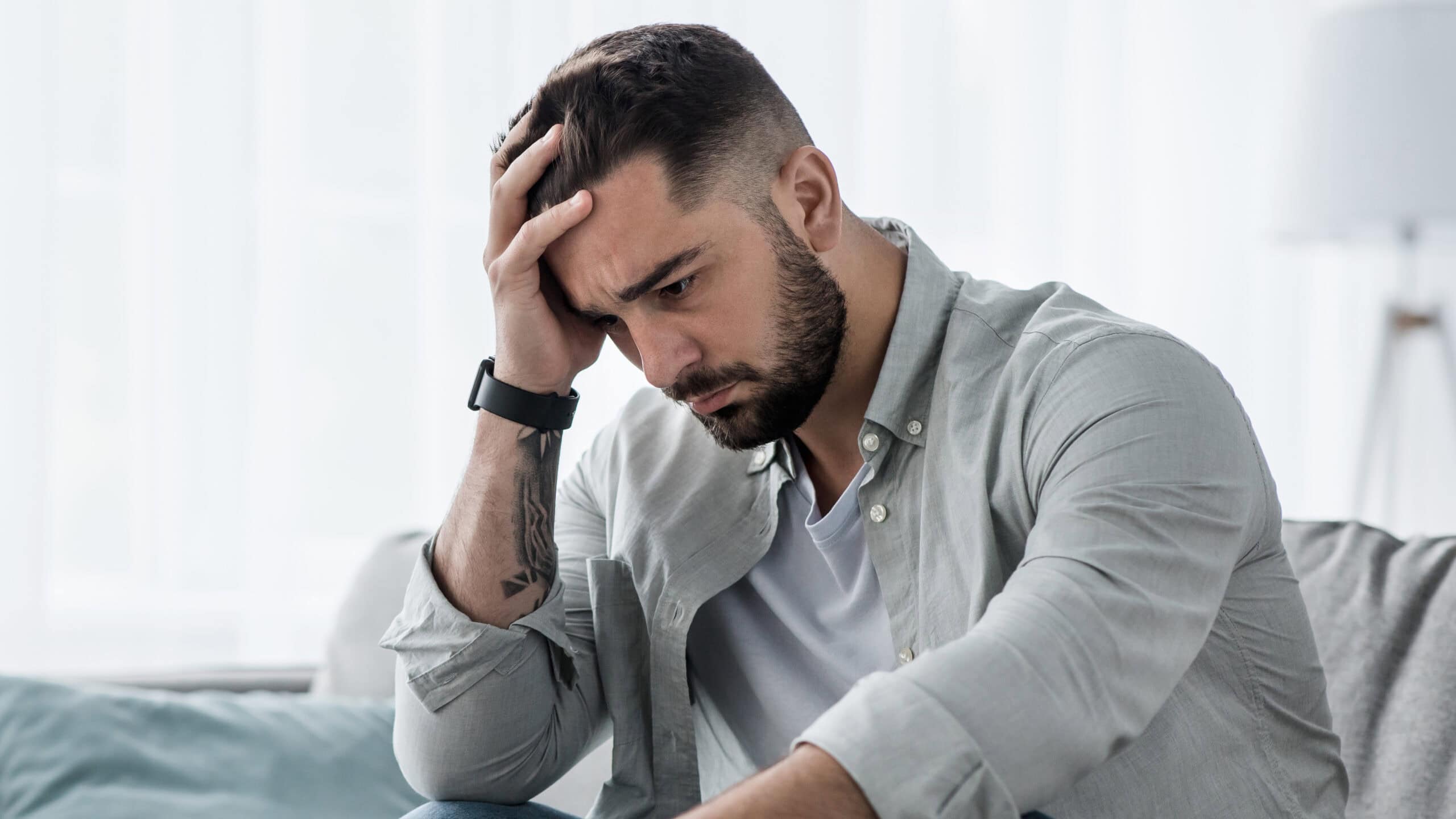 Sudden headache and stress affecting mental health, young man in distress holding his head in a modern wellness clinic setting.