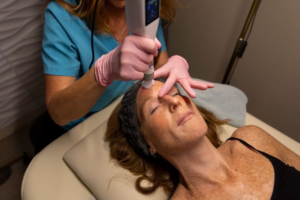 Aesthetic professional performing a skin rejuvenation procedure using a specialized device on a patient's face in a medispa setting.
