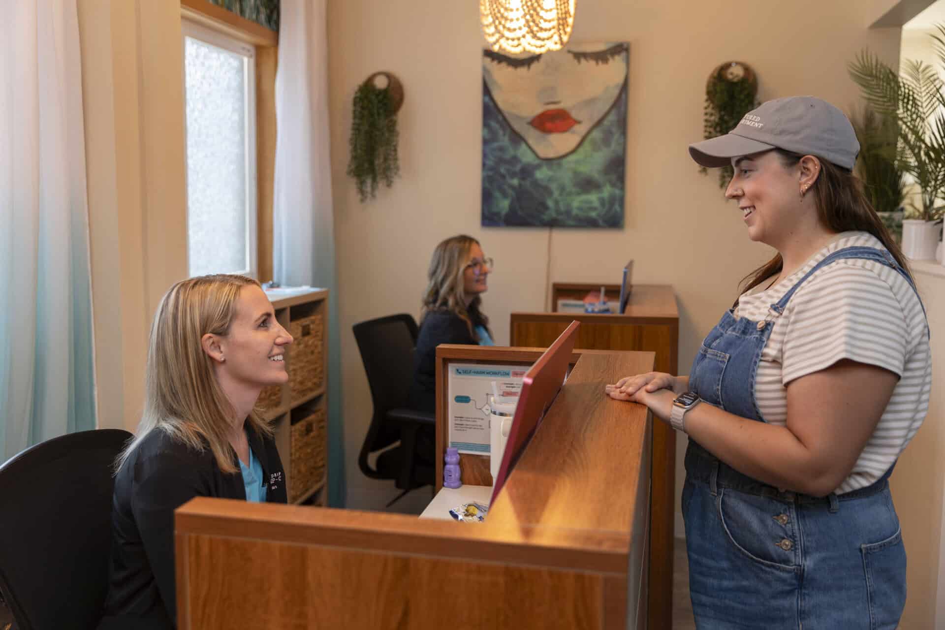 A woman at the reception desk of The Wellness Drip INC wellness clinic in MA, engaging with staff for health and wellness services.