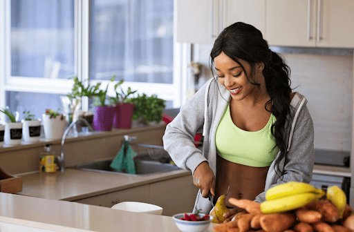 Healthy woman preparing a smoothie with bananas and vegetables in a modern kitchen at The Wellness Drip INC, a wellness clinic in MA offering IV therapy, Ketamine, Weight Loss and Wellness services.