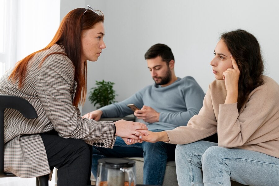 Feeling distressed during therapy session with a woman holding the hand of a young woman in a mental health counseling setting.