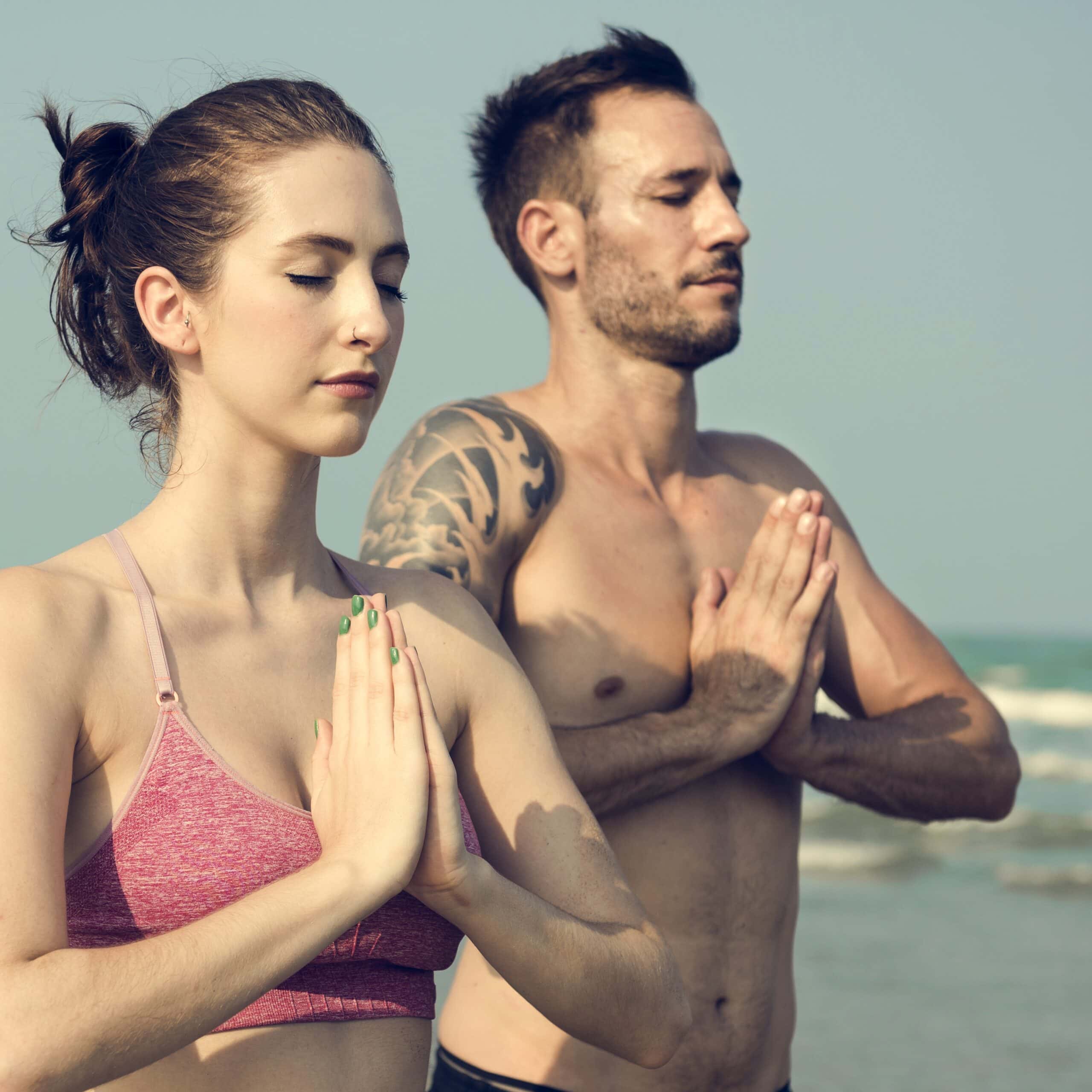 Serene young woman and man practicing yoga meditation on the beach, focusing on mental wellness and stress relief, with a calming ocean background.