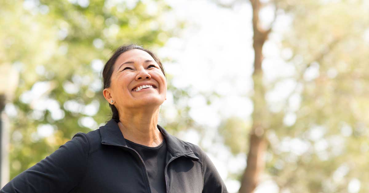 Vibrant woman smiling outdoors in a park, promoting mental and physical wellness services like Ketamine Therapy, IV vitamin infusions, and weight loss solutions at The Wellness Drip INC.