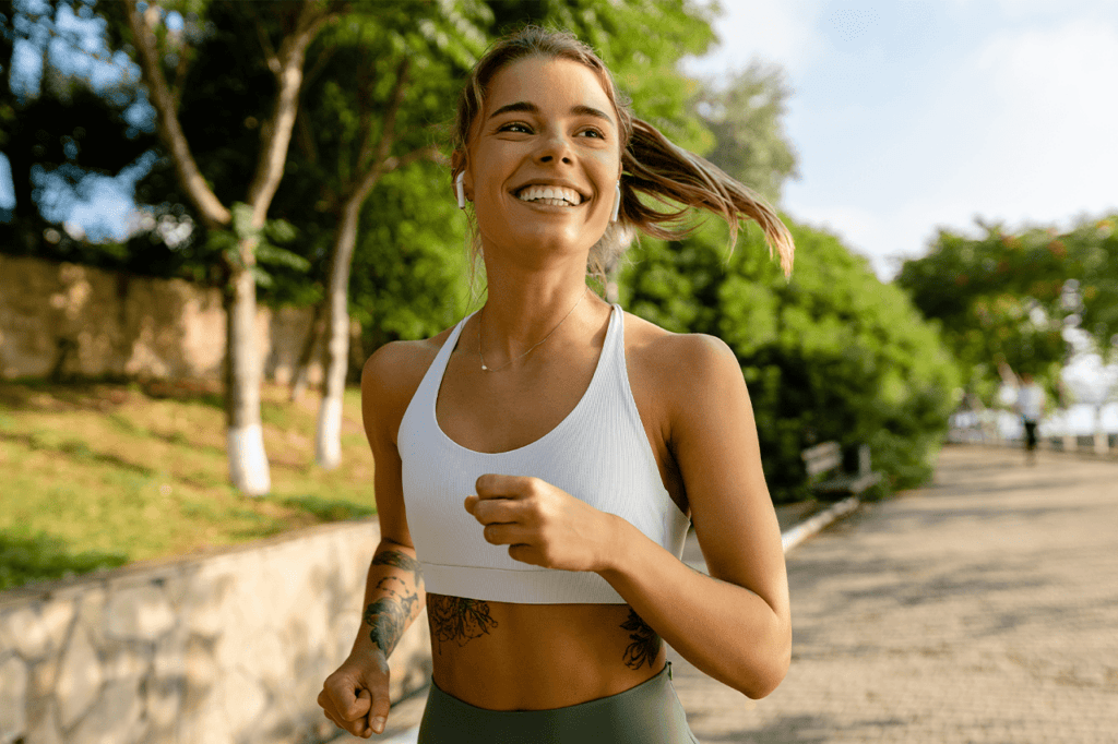 Vibrant young woman jogging outdoors in a park with trees, enjoying a healthy lifestyle and wellness activities offered by The Wellness Drip INC in MA.
