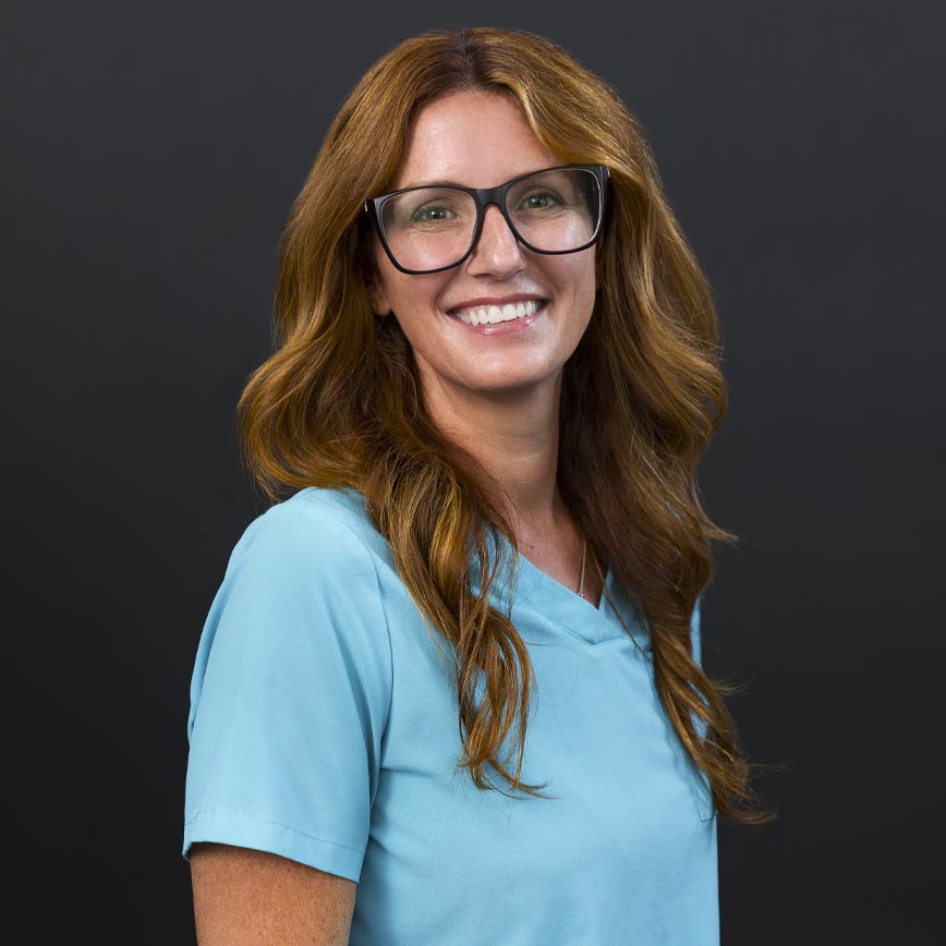 Kelley, smiling in a light blue medical uniform, representing wellness and expert care at The Wellness Drip INC.