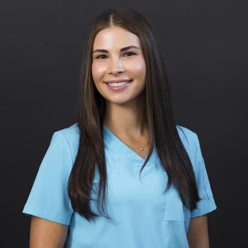 Alyssa in light blue medical scrubs smiling, healthcare professional at wellness clinic in MA, specializing in ketamine therapy, NAD+ infusions, and wellness services.