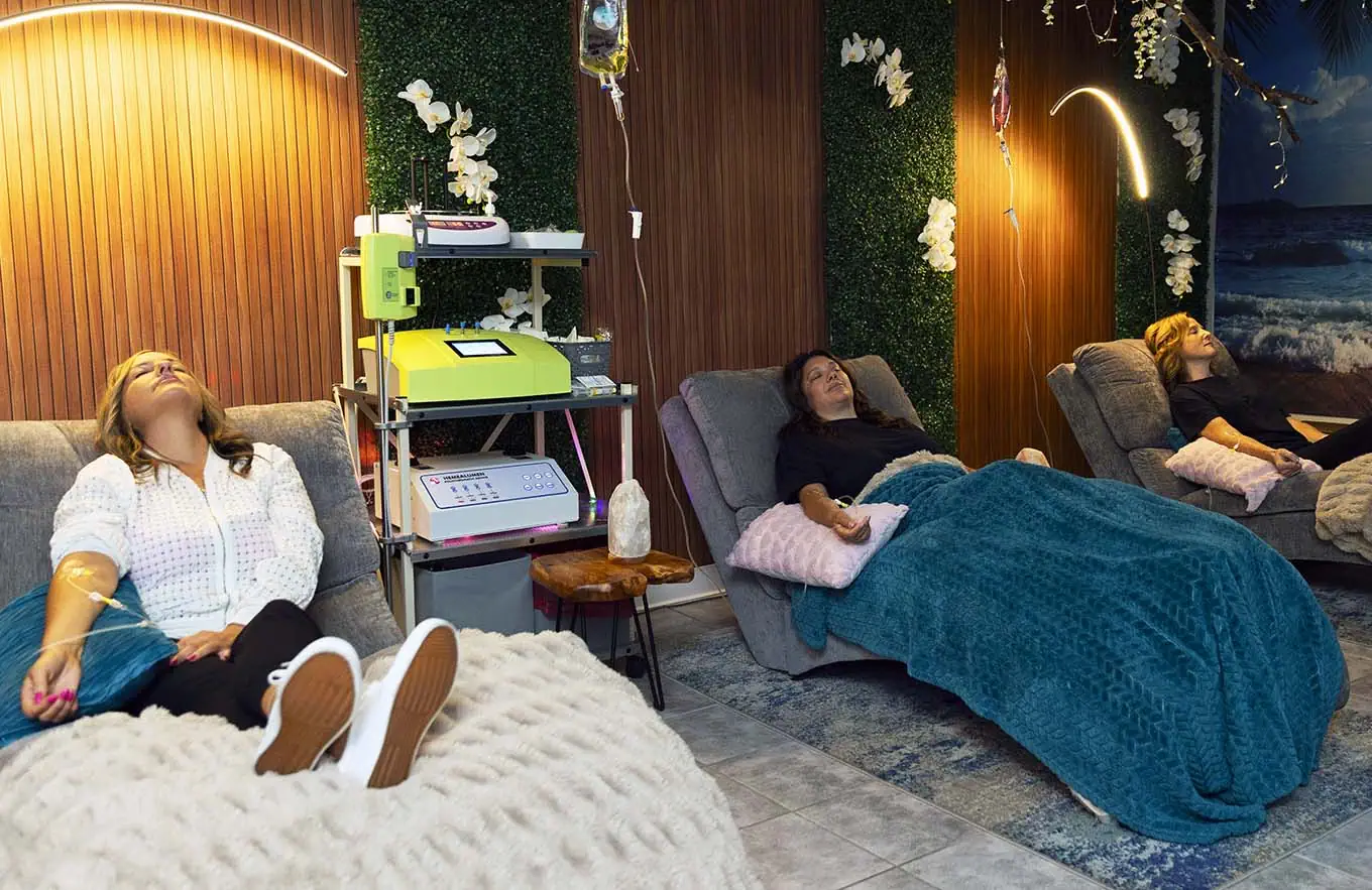 Soothing women receiving IV vitamin infusion therapy at wellness clinic in cozy, relaxing lounge.