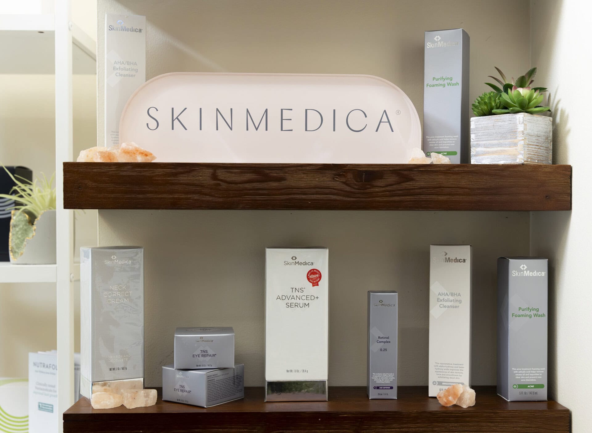 Skincare products including SkinMedica anti-aging serums and exfoliating cleansers displayed on wooden shelves at The Wellness Drip INC wellness clinic in MA.