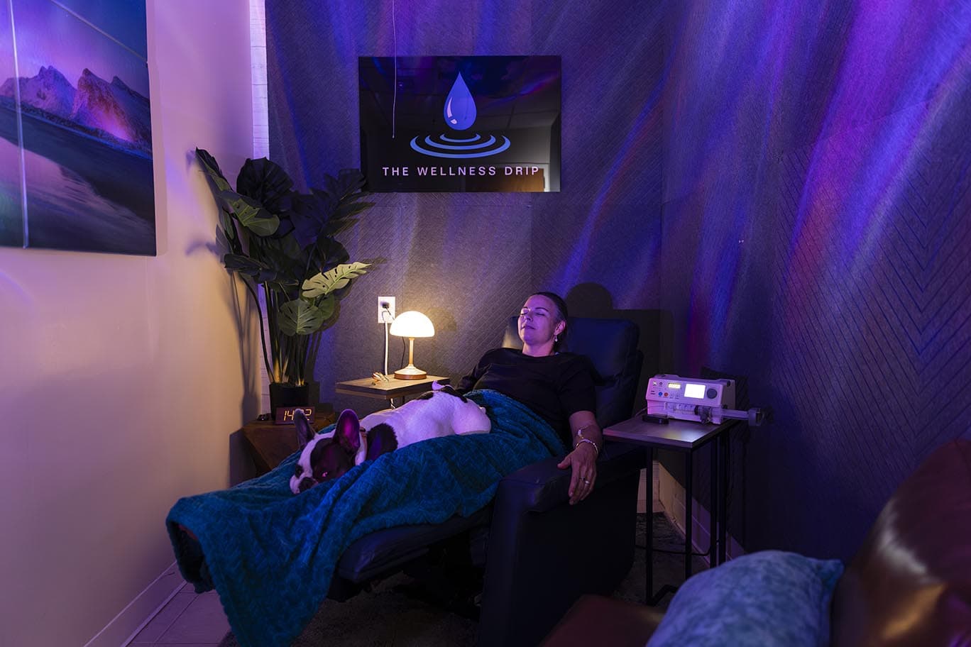 Calming wellness clinic room with a woman relaxing, IV therapy, mood lighting, and a therapy device at The Wellness Drip INC, MA, specializing in ketamine therapy and wellness treatments.