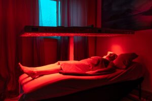 A person lying comfortably on a wellness therapy bed under red LED light, promoting health and relaxation at The Wellness Drip INC. Illustration of full body red light therapy session