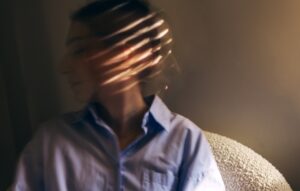 A woman sitting on a couch with light patterns on her face, symbolizing mental health treatment and wellness therapy at The Wellness Drip INC, specializing in OCD and ketamine therapy.