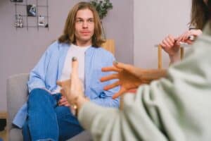 A young man with shoulder-length hair sitting on a sofa during an IV therapy consultation at Wellness Drip Holyoke, discussing health and wellness options with a healthcare professional.