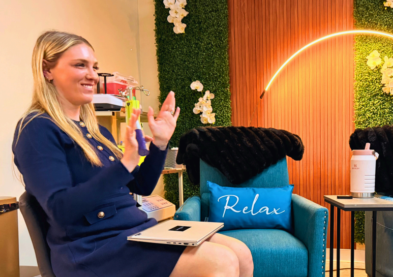 A woman enjoying a relaxing aesthetic treatment at Wellness Drip Holyoke, with a cozy, modern setting featuring green wall decor and a "Relax" pillow.